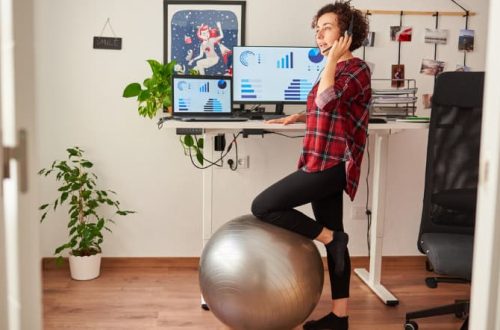 how to reduce the effects of sitting all day - woman standing up at a standing desk with a knee resting on her stability ball